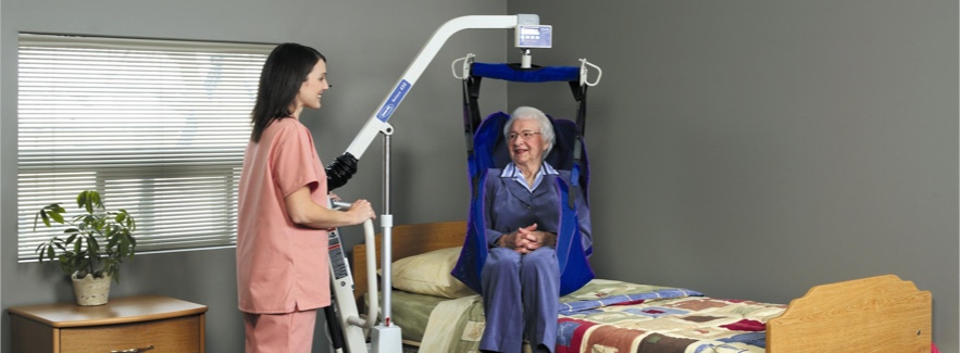 A woman helping an elderly woman out of bed with a lift.