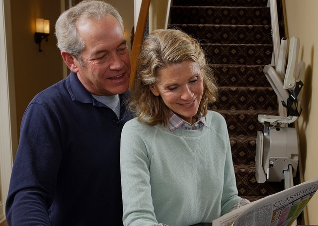 a happy couple reading the newspaper with a stairlift in the background