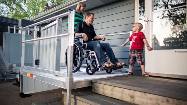A man in a wheelchair with his wife and son using the EZ-ACCESS PASSPORT® Vertical Platform Lift