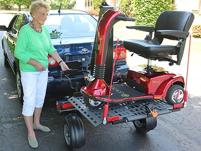 A woman standing beside a scooter on a chariot attached to a car