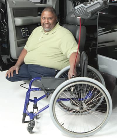 A man sitting in a truck with a scooter beside him