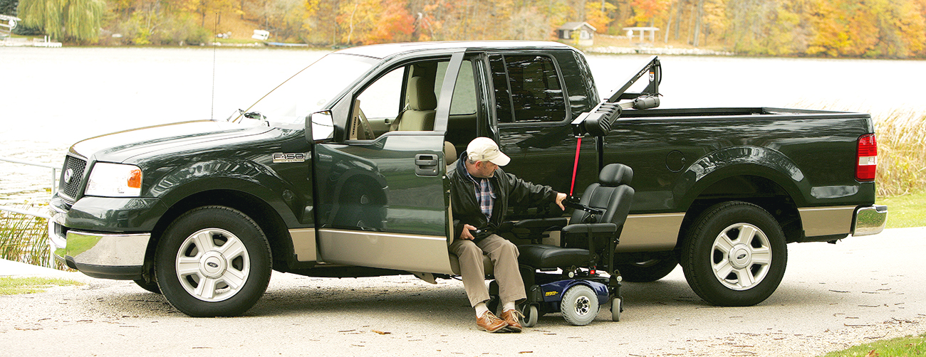 A man sitting in a truck with a scooter beside him