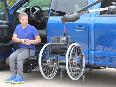 A man sitting in a truck with a scooter beside him
