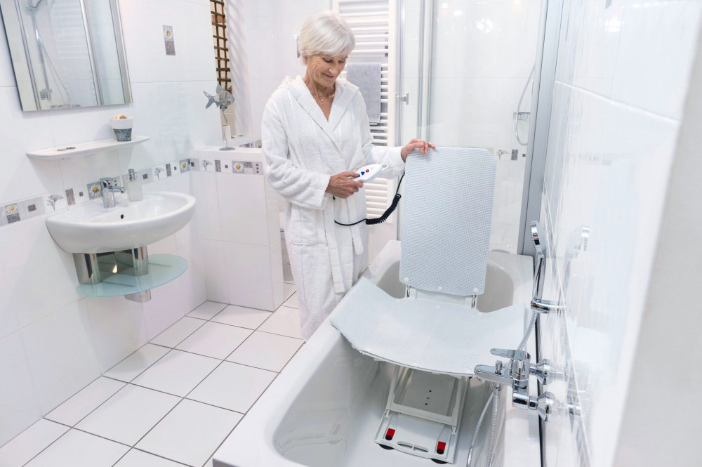 Woman standing beside a bathtub with a bath lift in the tub.